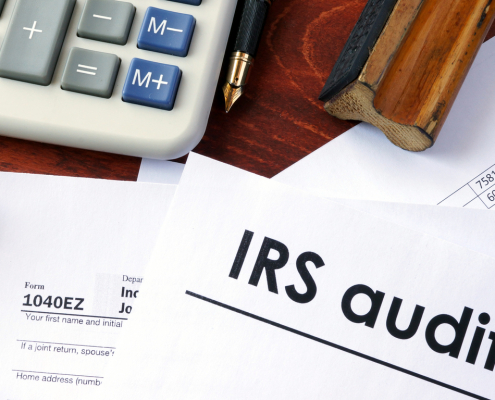 a desk with tax forms, a calculator, glasses, and a form saying irs audit