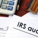 a desk with tax forms, a calculator, glasses, and a form saying irs audit