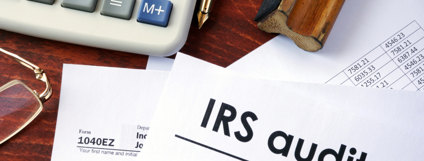 a desk with tax forms, a calculator, glasses, and a form saying irs audit