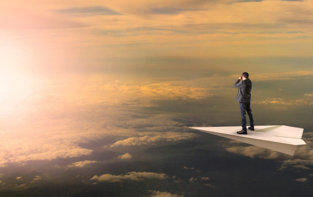 Business owner standing on a paper airplane high above the clouds, looking into the distance as a metaphor for planning and forward-looking tax strategy.