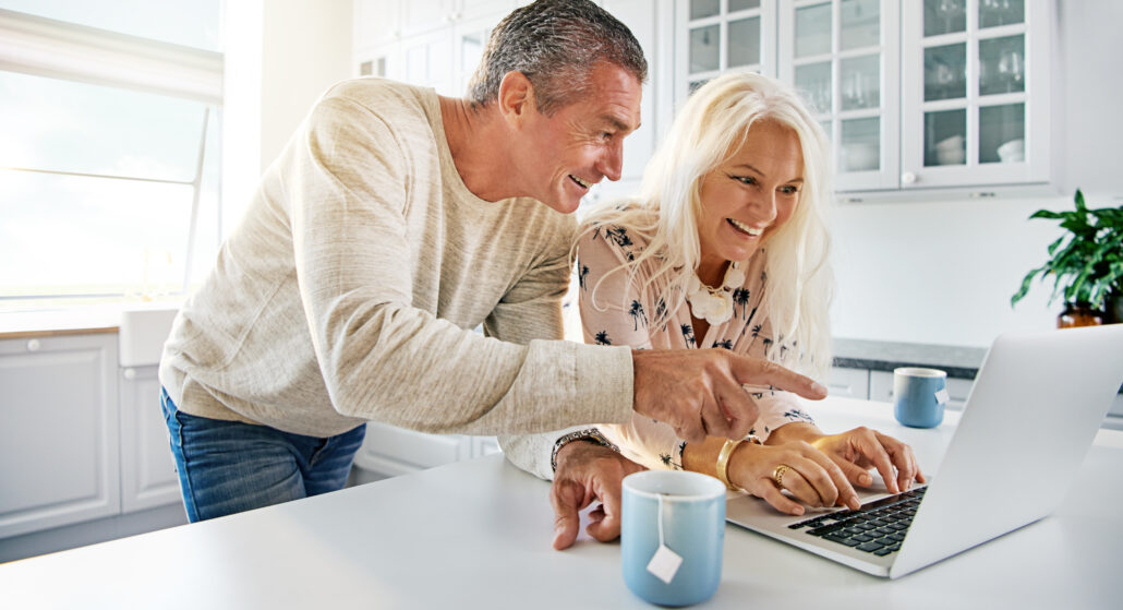 Smiling mature couple at kitchen counter reviewing retirement tax planning on a laptop